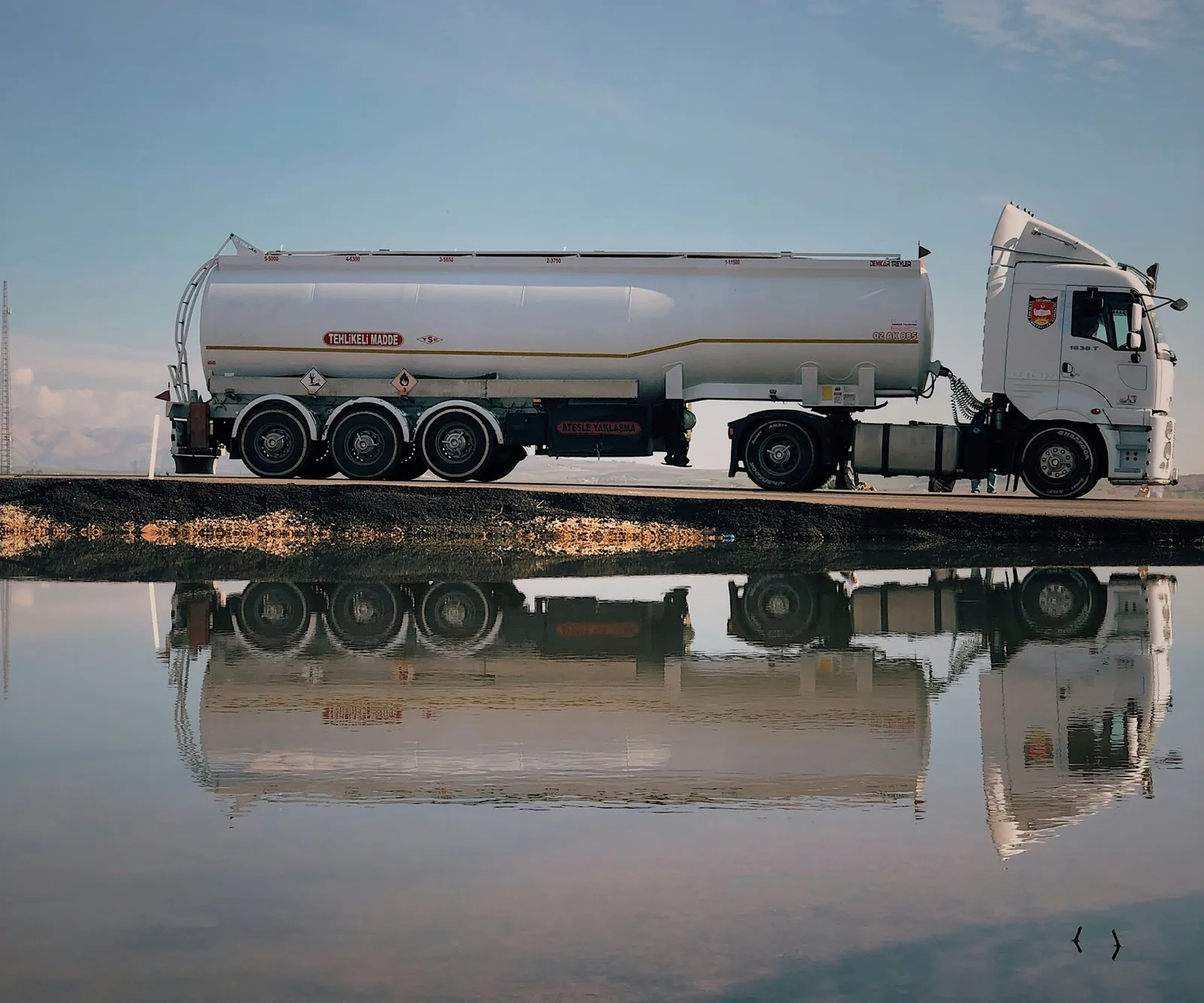 Fuel tanker truck on a road, reflected in still water